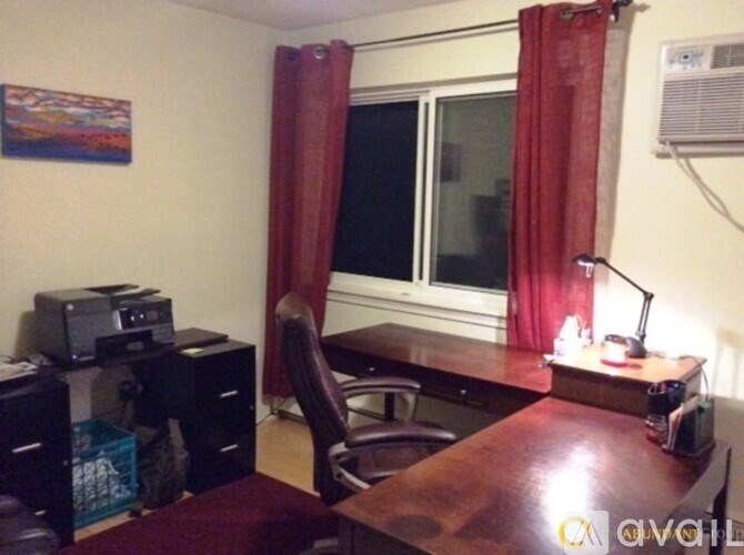 A room with a desk, chair, and a window with red curtains.