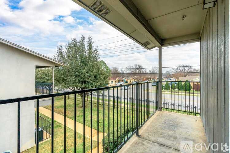 A balcony with a black railing overlooks a grassy area and a road.