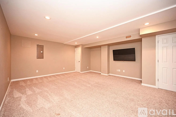A spacious room with a carpeted floor and a flat-screen TV mounted on the wall.