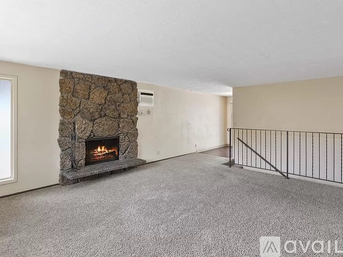 A living room with a stone fireplace and grey carpet.