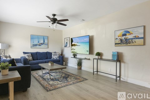 A living room with a blue couch and a painting of a beach scene on the wall.