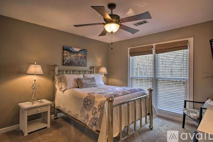 A bedroom with a bed, a ceiling fan, and a painting on the wall.