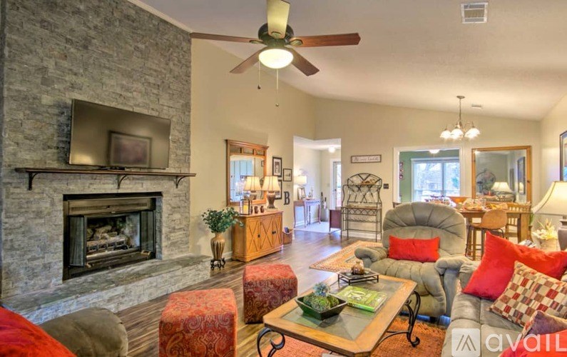 A living room with a stone fireplace and a ceiling fan.