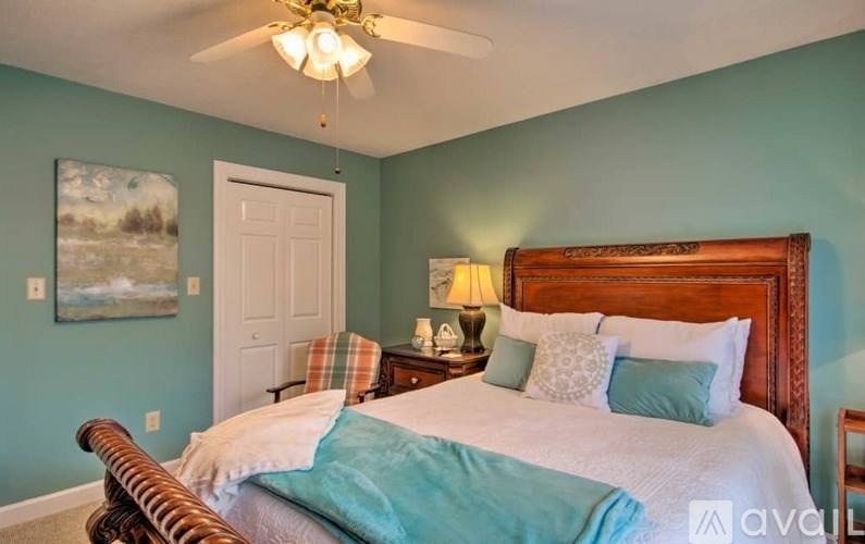 A bedroom with a bed, a ceiling fan, and a painting on the wall.
