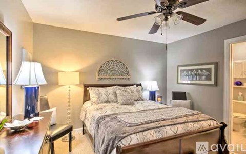 A bedroom with a bed, a ceiling fan, and a nightstand with a lamp.