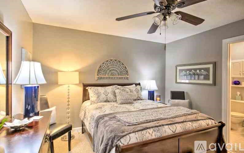 A bedroom with a bed, a ceiling fan, and a nightstand with a lamp.