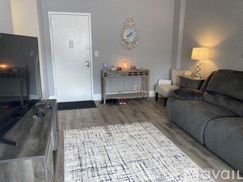 A living room with a grey couch, a coffee table with candles, and a clock on the wall.