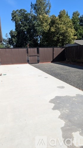 A concrete area with a brown fence and trees in the background.