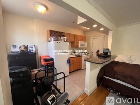 A bedroom with a bed, dresser, and a kitchenette with a refrigerator and microwave.