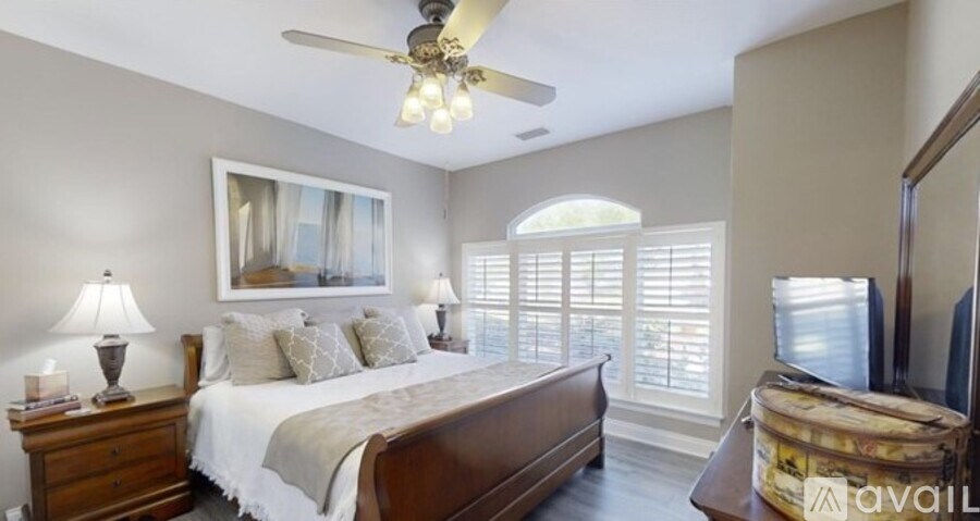 A bedroom with a large bed, a ceiling fan, and a painting on the wall.