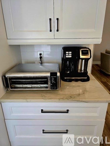 A black coffee maker sits on a marble countertop.