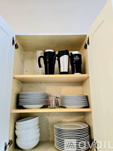 A kitchen cabinet with plates and cups on the shelves.