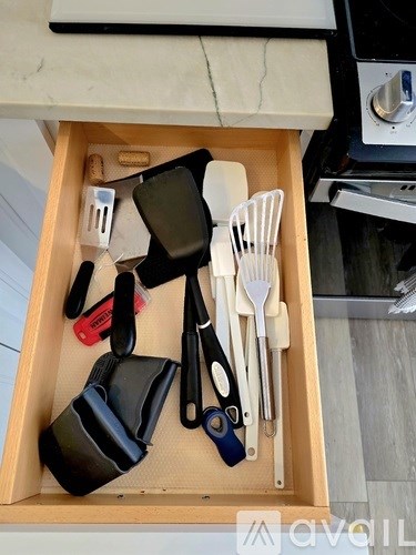 A drawer with utensils and a black container.