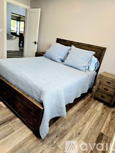 A bed with a blue bedspread and two pillows is in the foreground with a wooden headboard.