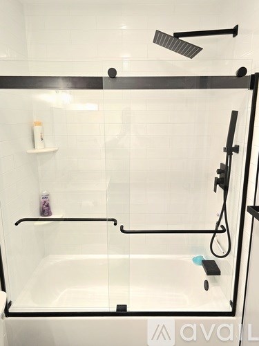 A white bathroom with a glass shower door and a black handle.