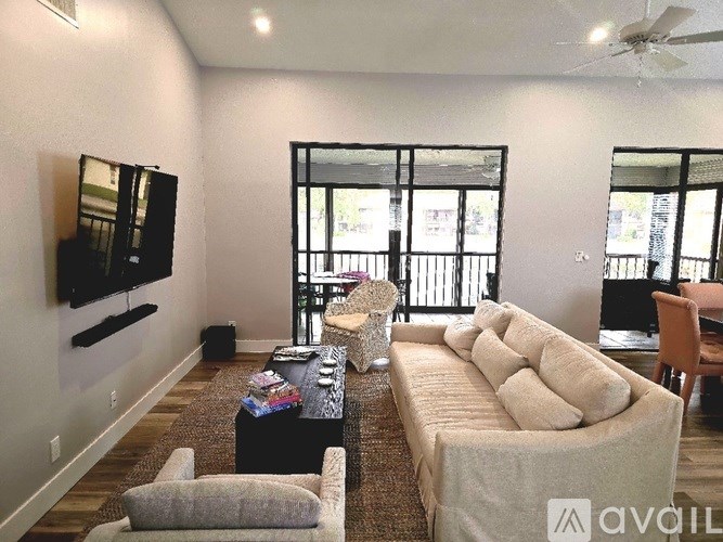 A living room with a white couch, a black coffee table, and a flat-screen TV mounted on the wall.