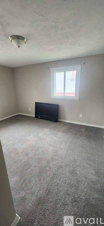 A room with a grey carpet and a window.