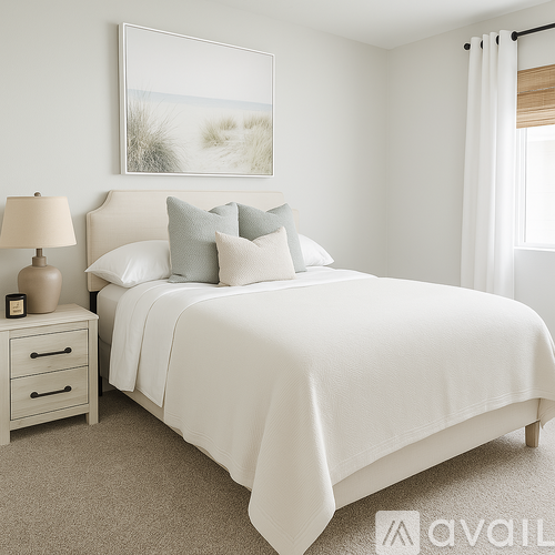 A white bedroom with a large bed and a painting on the wall.