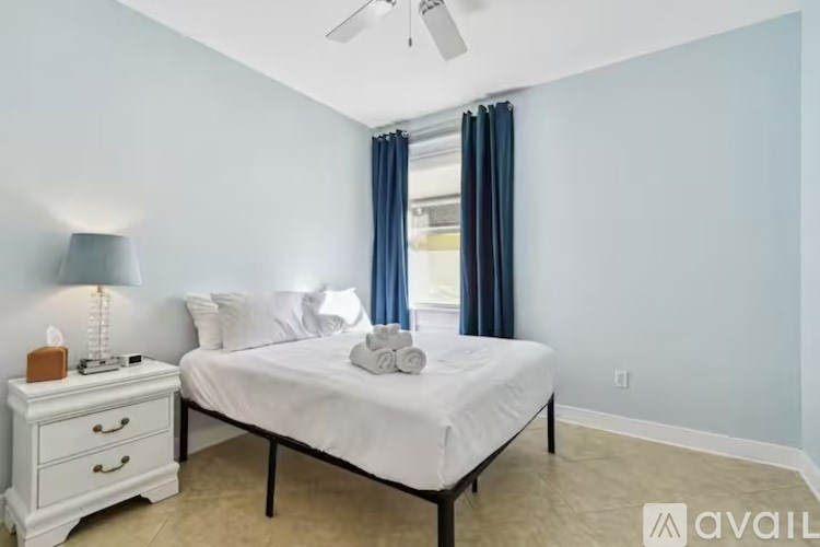 A bedroom with a bed, nightstand, and window with blue curtains.