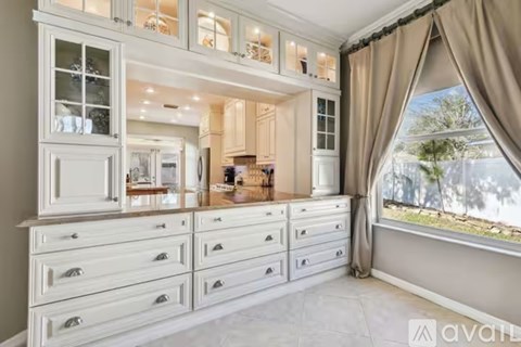 A kitchen with white cabinets and drawers, a window with curtains, and a view of trees outside.