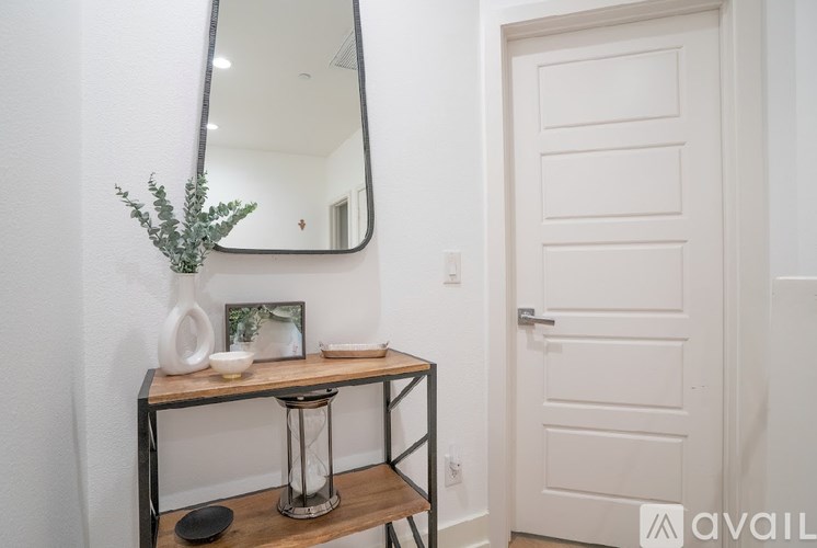 A white door is next to a mirror and a table with a vase and picture frame on it.