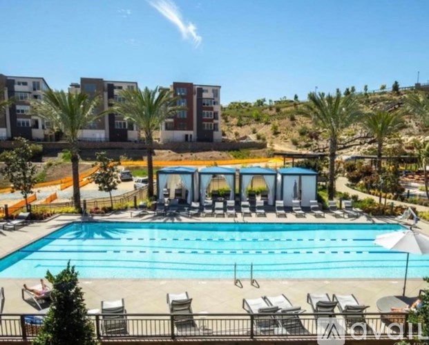 A large swimming pool surrounded by lounge chairs and umbrellas with apartment buildings in the background.