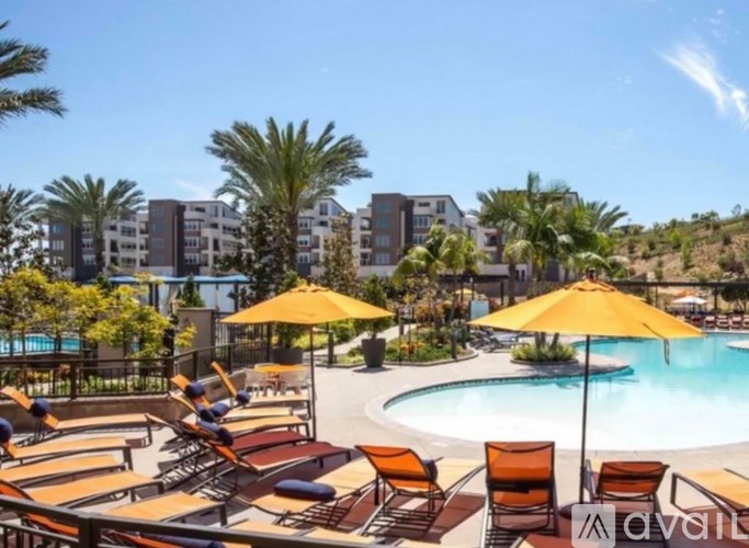 A pool area with sun loungers and umbrellas in front of apartment buildings.