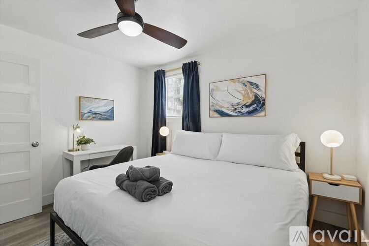 A bedroom with a bed, a desk, a ceiling fan, and two wall art pieces.
