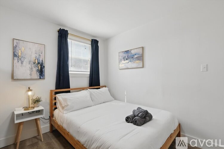 A bedroom with a bed, nightstand, and two paintings on the wall.