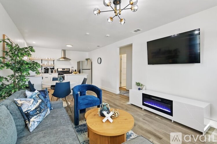 A living room with a grey couch, a blue chair, a wooden coffee table, and a flat screen TV mounted on the wall.