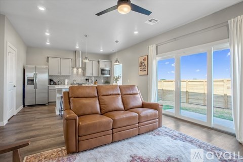 A brown leather sofa sits in a well-lit living room with a kitchen in the background.