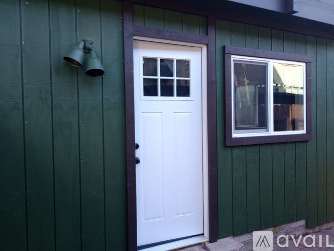 A white door is on the left of a window on a green building.