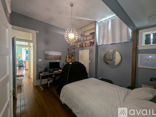 A bedroom with a large bed and a workspace with a computer and guitar.