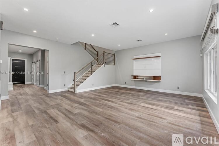 A spacious room with wooden flooring and a staircase.