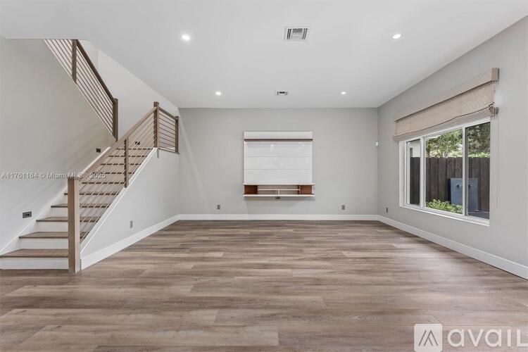 A spacious room with wooden flooring and a staircase on the left side.