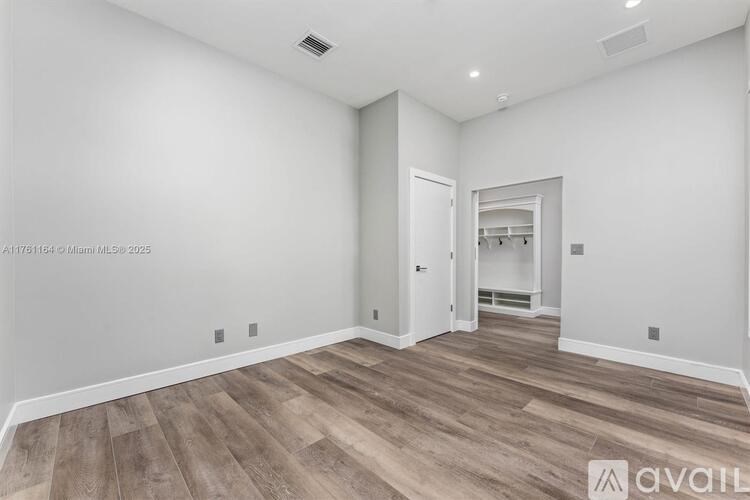 A room with wooden flooring and white walls, with a doorway leading to another room.