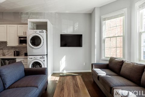 A modern living room with a grey couch and a washing machine built into the cabinet.