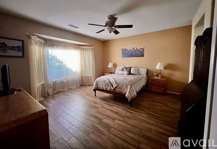 A bedroom with a bed, a ceiling fan, and a window with curtains.