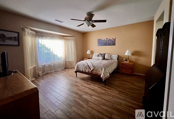A bedroom with a bed, a ceiling fan, and a window with curtains.