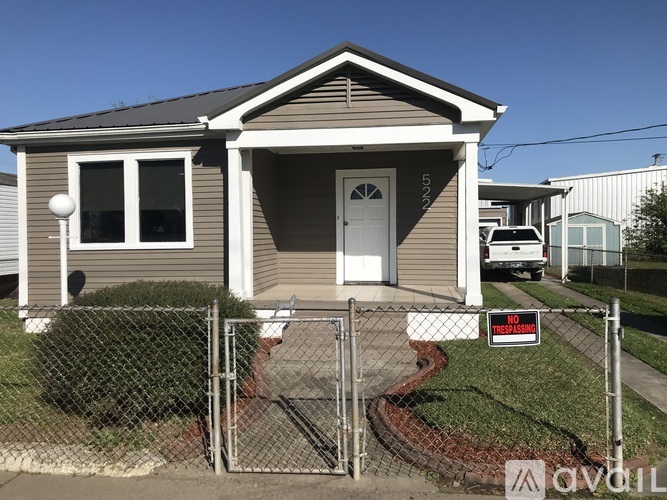 A house with a grey siding and a white door is surrounded by a fence with a "No Trespassing" sign.