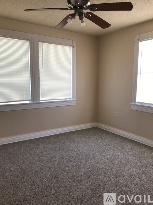 A room with a ceiling fan and two windows.