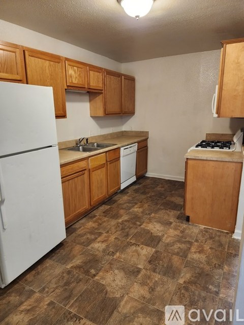 A kitchen with a white refrigerator, brown cabinets, and a brown tiled floor.