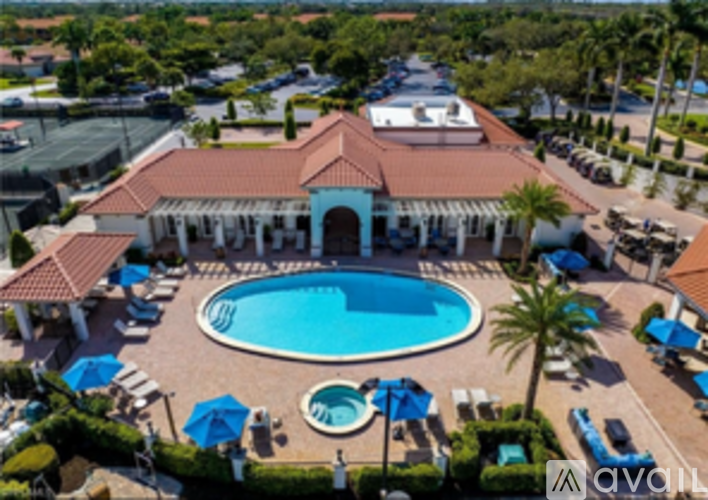 A pool surrounded by a patio with chairs and a building in the background.