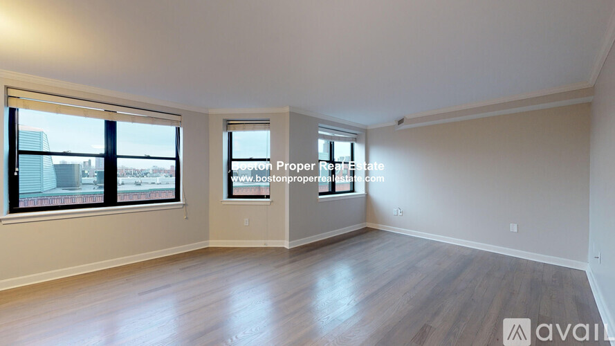A spacious room with wooden flooring and two windows overlooking a cityscape.