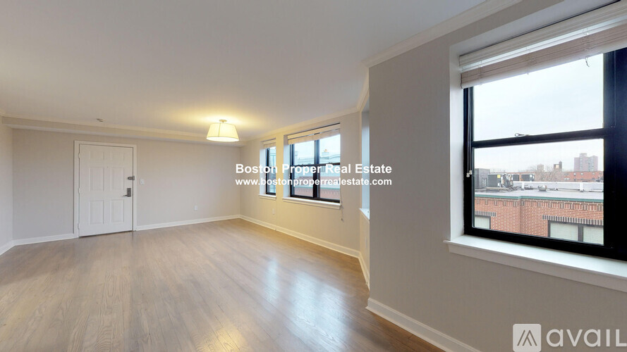 A spacious room with wooden flooring and a large window overlooking a cityscape.