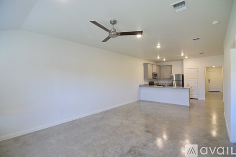A spacious room with a ceiling fan and a kitchenette in the background.