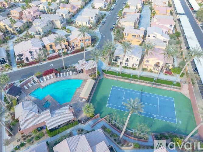 A tennis court is surrounded by houses and palm trees.