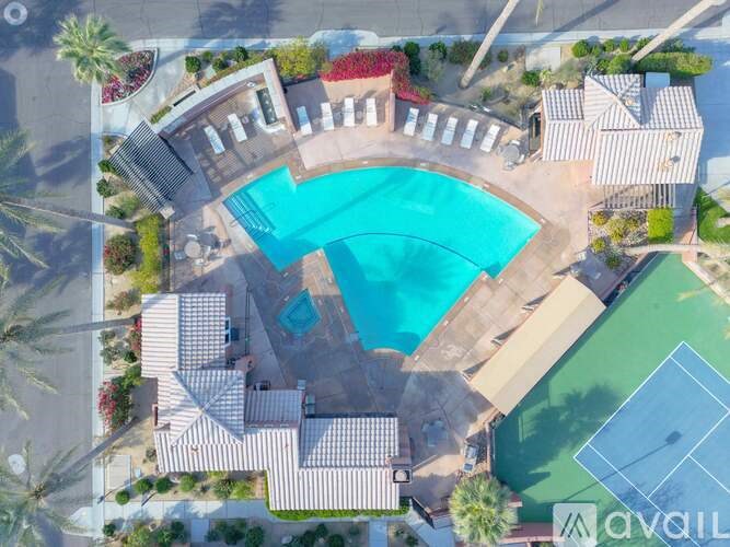 An aerial view of a pool surrounded by a tennis court and palm trees.