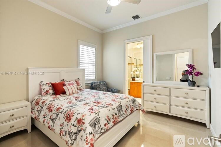 A bedroom with a floral bedspread, a white bed, a dresser, and a mirror.