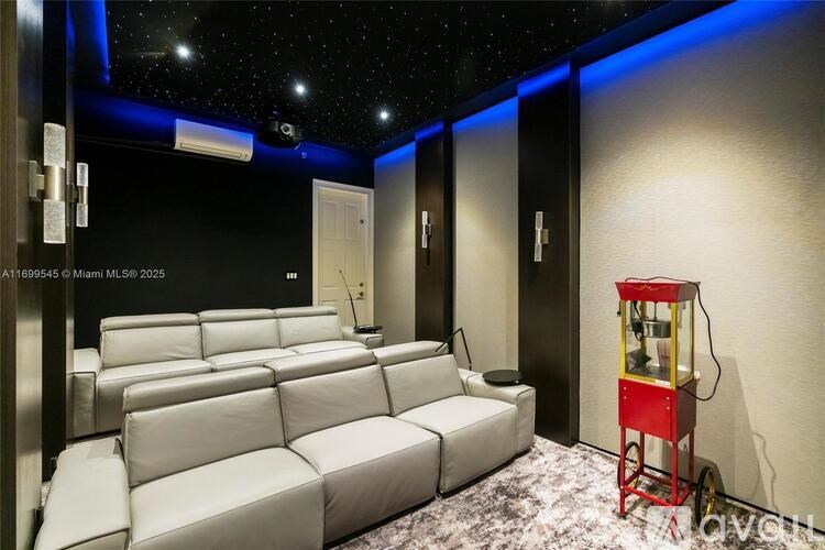 A home theater room with a row of white leather seats and a red popcorn machine.